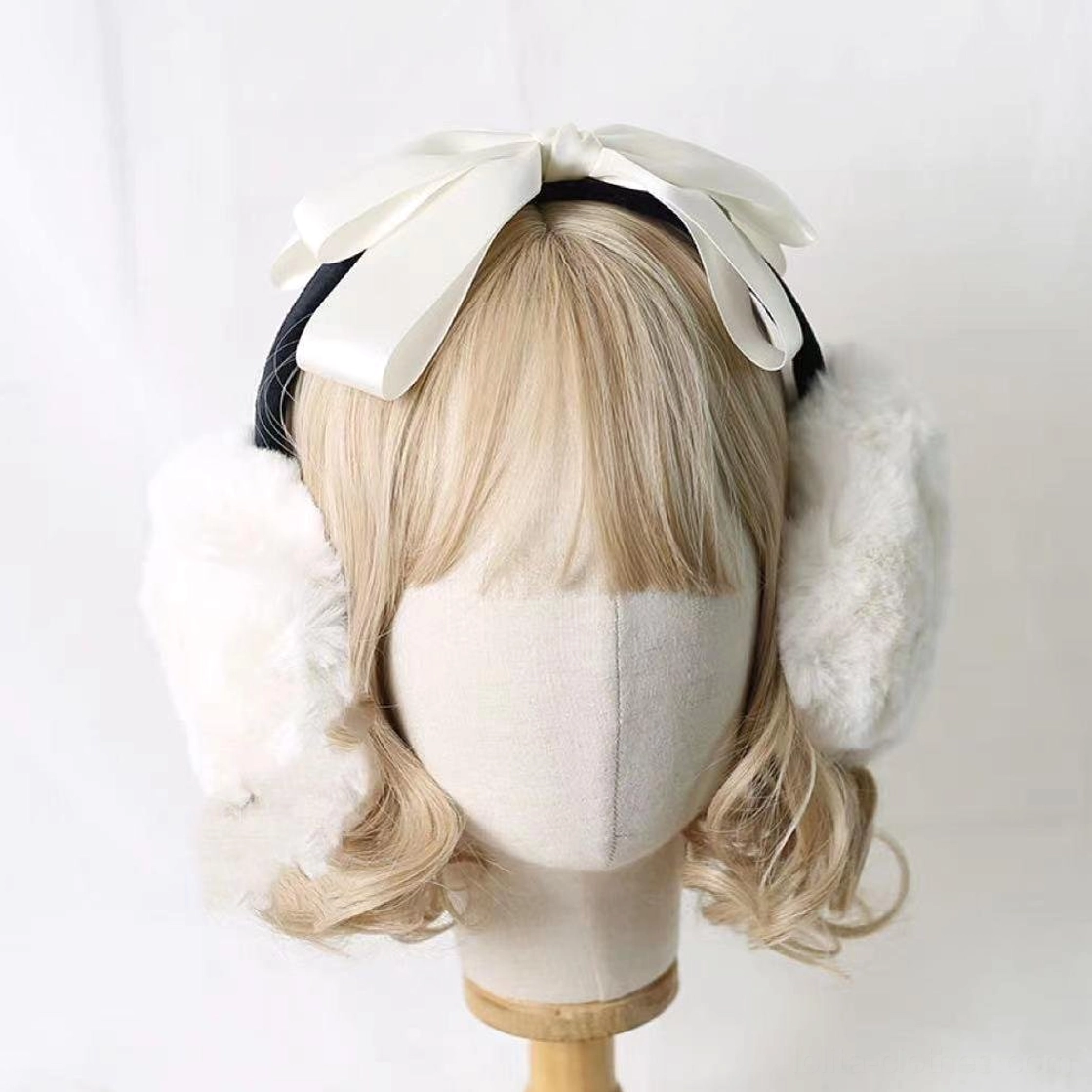 Lolita plush earmuff headdress styled on blonde mannequin, off-white cream satin bow with white fuzzy earmuff cups, black headband base, front view