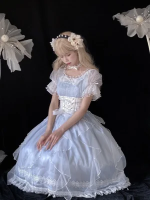 Sweet Lolita OP dress overhead sitting view showing square neckline, layered organza skirt, white lace bottom trim, and mesh bubble sleeves with model wearing flower headpiece in studio setting