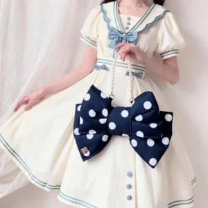 Lolita fashion model wearing off-white sailor collar dress with detachable pearl chain crossbody bag strap styled with polka dot bow purse in cozy home interior setting with sheer white curtains