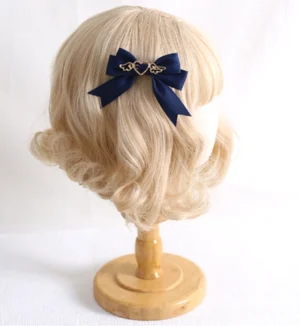 Handmade lolita satin bow hair clip with gold heart-wing charm displayed on blonde wig stand in navy blue
