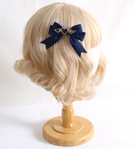 Handmade lolita satin bow hair clip with gold heart-wing charm displayed on blonde wig stand in navy blue