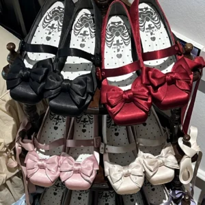 Stacked display of assorted lolita satin Mary Jane shoes in multiple colors including black burgundy pink and off-white with matching satin bows and branded insole
