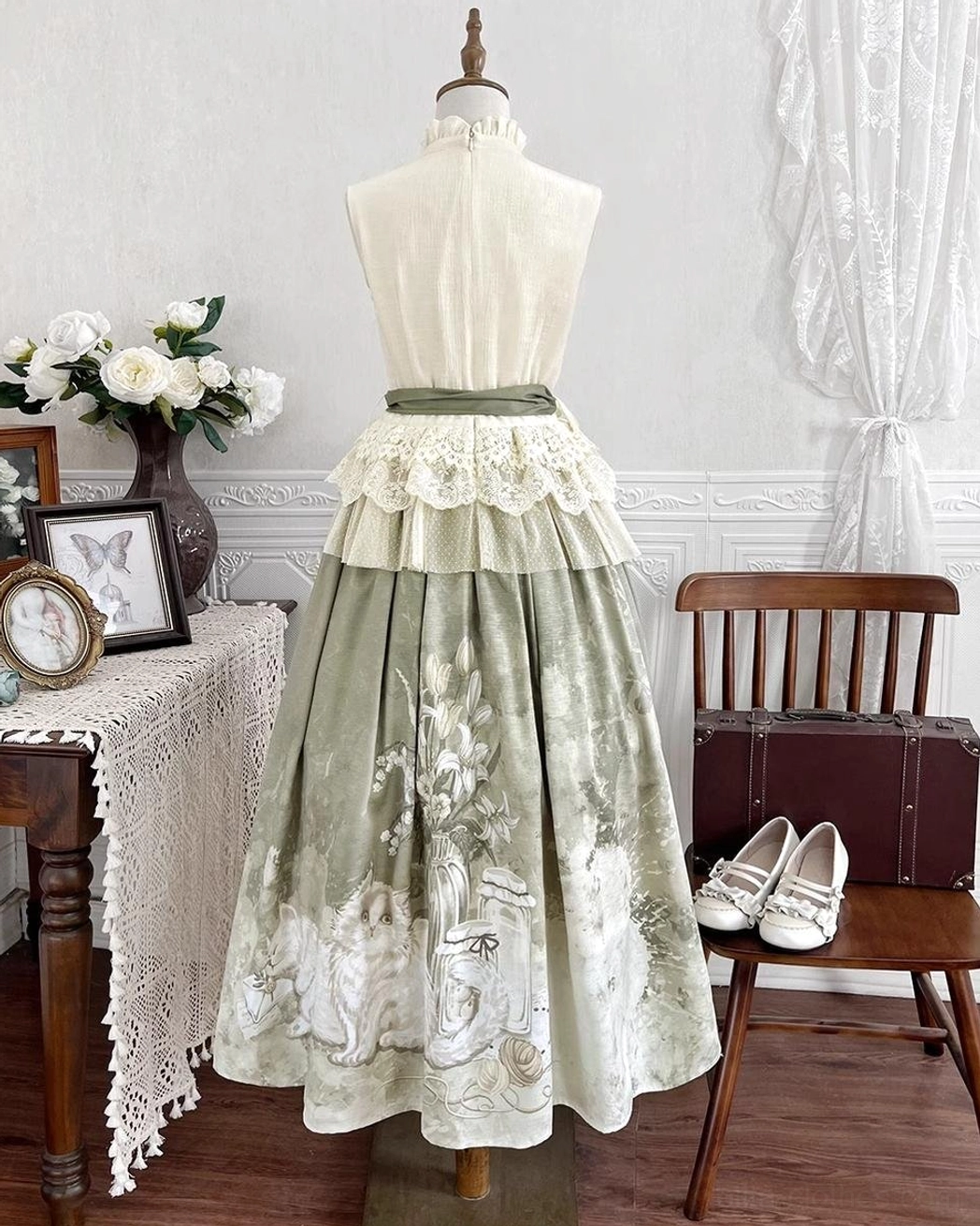 Three-quarter front view of matching lolita ensemble showing tea-length skirt with floral and feline botanical print pattern and cream ruffled blouse on dress form
