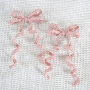 Pink lolita spiral bow hair clips pair flat lay top-down view showing classic bow shape with long curly ribbon tails and ruffled edges on white waffle textured fabric background