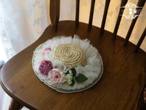 overhead flat lay of round woven straw lolita boater hat with white ruffled fabric border and mixed pastel rose blooms