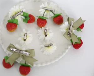 Sweet lolita strawberry daisy hair clips flat lay on decorative ceramic tray showing red glittery strawberry charms with white daisy flowers and sage green ribbon bows