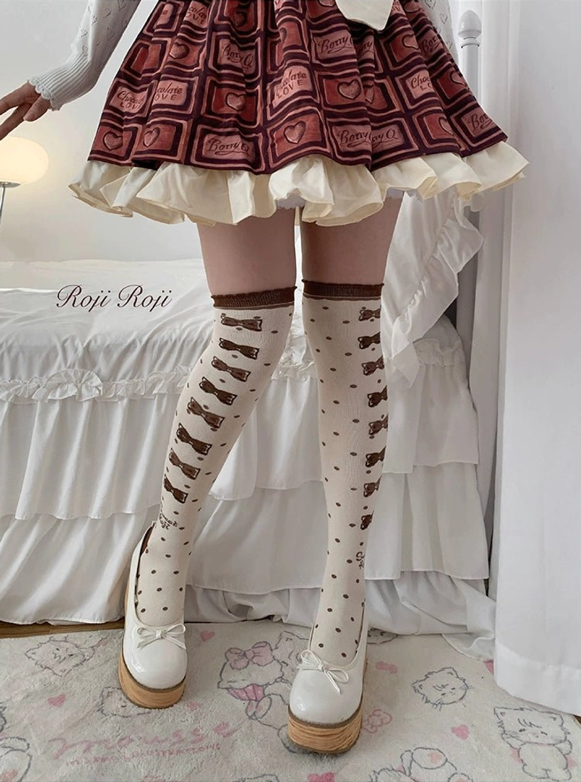 Lolita thigh-high over-the-knee socks brown and coffee bow print cream base worn with red heart-print lolita skirt white platform loafers indoor bedroom full leg view