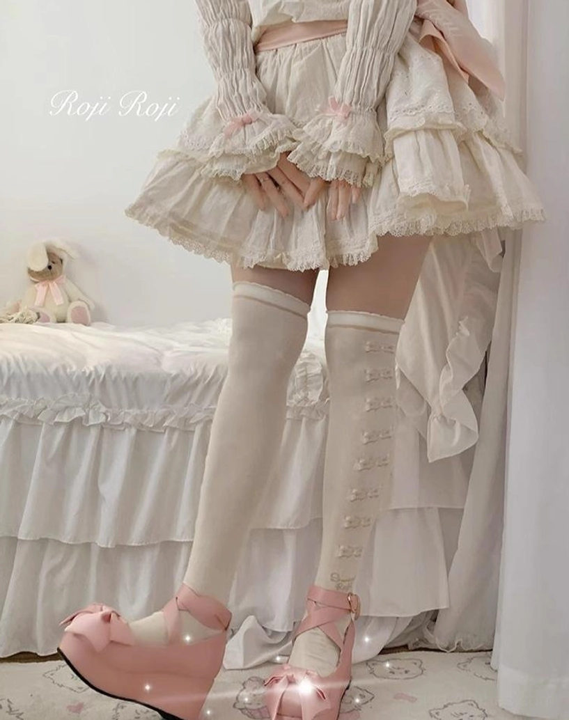 Lolita thigh-high socks cream base vertical bow lace trim pattern slim fitted leg silhouette beige ruffled skirt pink platform heels three-quarter side view