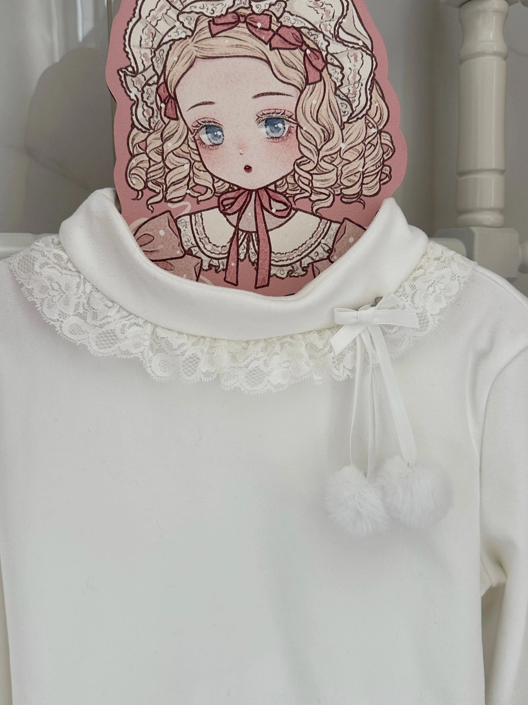 Extreme close-up detail of Lolita inner top collar featuring lace ruffled turtleneck, tiny fabric bow, and fluffy pompom trims with vintage character sign backdrop