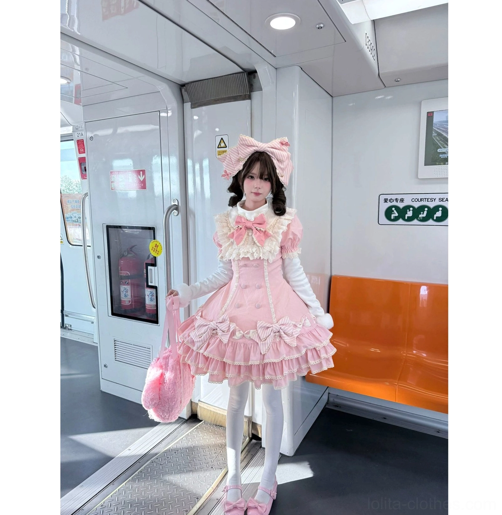 Model wearing matching pink sweet Lolita set with pompom winter innerwear base layer in subway station photoshoot with big bow headpiece and handbag