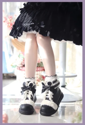 Black and white lolita winter ankle boots with bow lace-up closure and fluffy white plush trim, worn with black ruffled skirt in floral photography studio