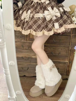 Side mirror view of model wearing cream lolita winter plush boots paired with beige knitted leg warmers with bow decoration and brown plaid ruffle trim skirt, showcasing thick platform sole