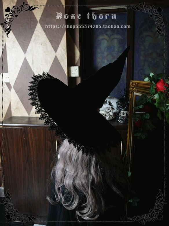 Rear back view of black velvet lolita witch hat on mannequin with curly wig, showing pointed hat top, lace-trimmed brim edge and ribbon tie in vintage indoor room