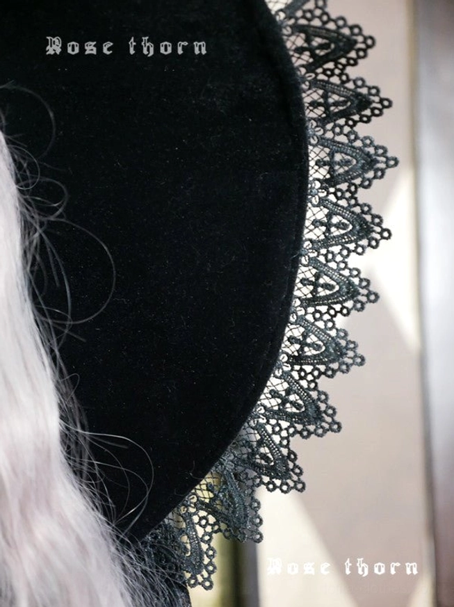 Side close-up view of delicate black floral lace brim trim on smooth black velvet hat surface, showing product branding on fabric and lace embellishment detail