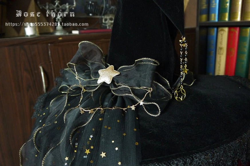 Close-up side top view of black satin bow with gold star chain and star pendant on lolita witch hat, star-printed sheer fabric detail