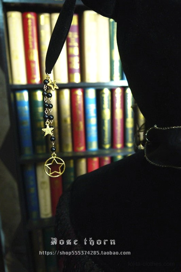 Close-up side view of gold star and pentagram metal tassel chains on black velvet lolita witch hat material