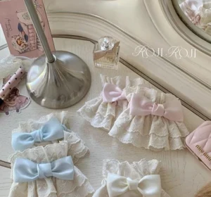 Elegant Sweet Lolita lace arm cuffs with scalloped layered lace trim and satin bow accents arranged on vintage dressing table with perfume bottle, greeting card, and pink wallet styling