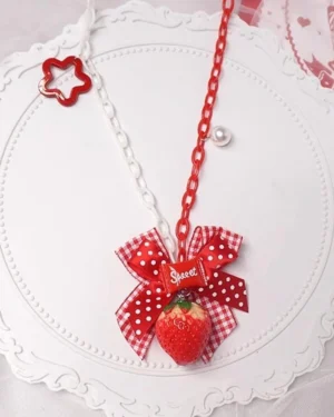 Long sweet lolita strawberry necklace close-up detail shot showing red white link chain pearl accent polka dot bow with sweet tag and large resin strawberry pendant on vintage decorative plate