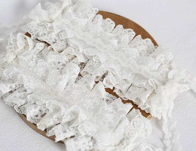 Loose lolita lace headdress band side flat lay view on white wooden base, cream white color with stacked ruffled lace and neat folded fabric design showing texture quality