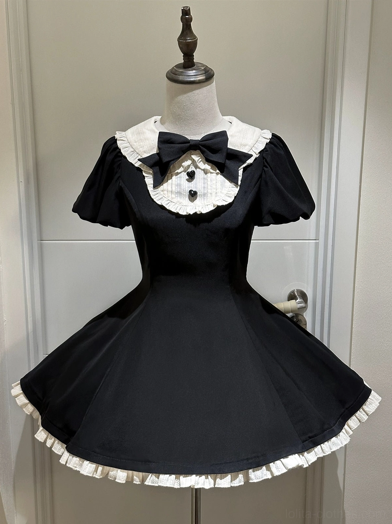Black base dress component of maidette lolita set on mannequin showing ruffled cream trim skirt hem large black bow at round collar and button bodice details