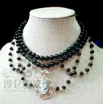 Manor Ball II black pearl cameo necklace front display view showing dark pearl strands with golden brown vintage portrait pendant and delicate framework detail