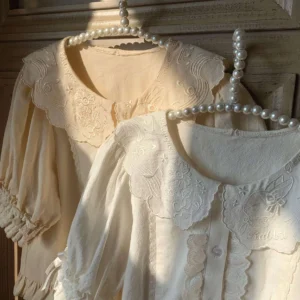 Two matching cream lolita cotton blouses with scalloped doll collars overhead view pearl hangers