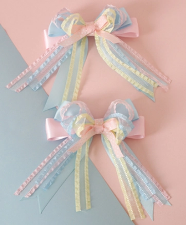 Two pairs matching pastel ribbon bow hair clips with tri-color ribbon design and long trailing tails flat lay oblique view