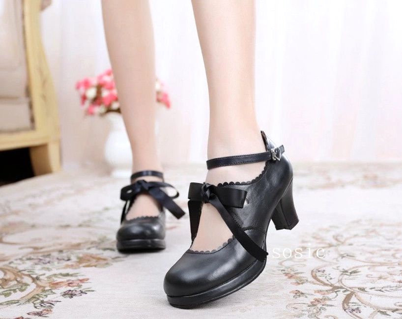 Matte black lolita high heel shoes with cross black ribbon bow, scalloped vamp, ankle buckle strap, and chunky block heel on floral carpet background in indoor setting