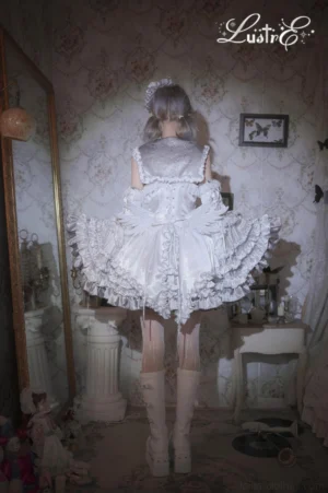 Back view of silver-white punk lolita JSK dress showing open back design, layered ruffled hem, matching feather hair accessory, white thigh-high stockings and platform boots in vintage mirror setting