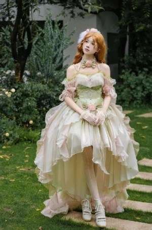 Green gradient wedding Lolita jumper skirt set with off-shoulder puff sleeves, corset bodice, flower decorations, and layered high-low skirt in outdoor garden setting