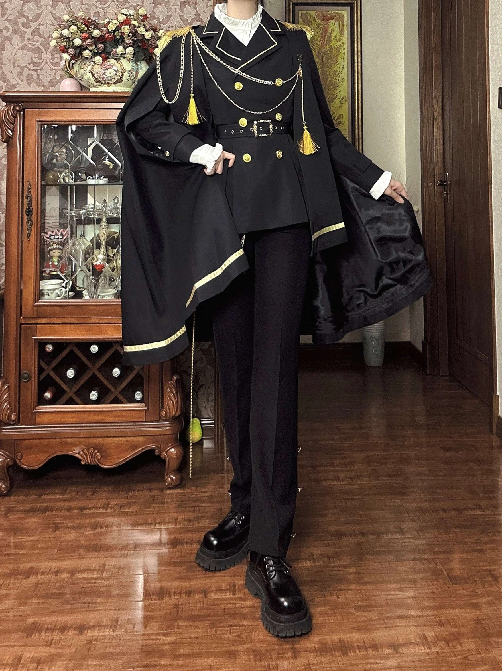 Full body front of military Ouji lolita wearing folded cape on arm with gold decorative buttons and thick-soled leather boots