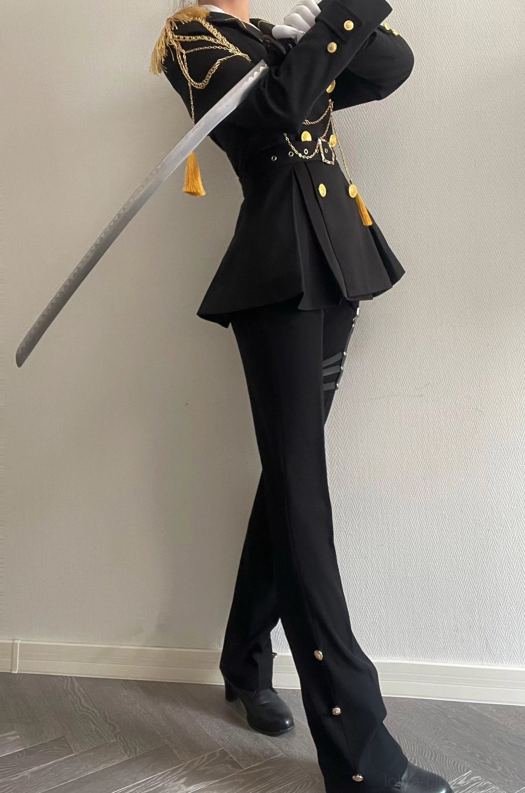 Low-angle side view of military Ouji lolita black tailored trousers with side buttons white gloves and coat details