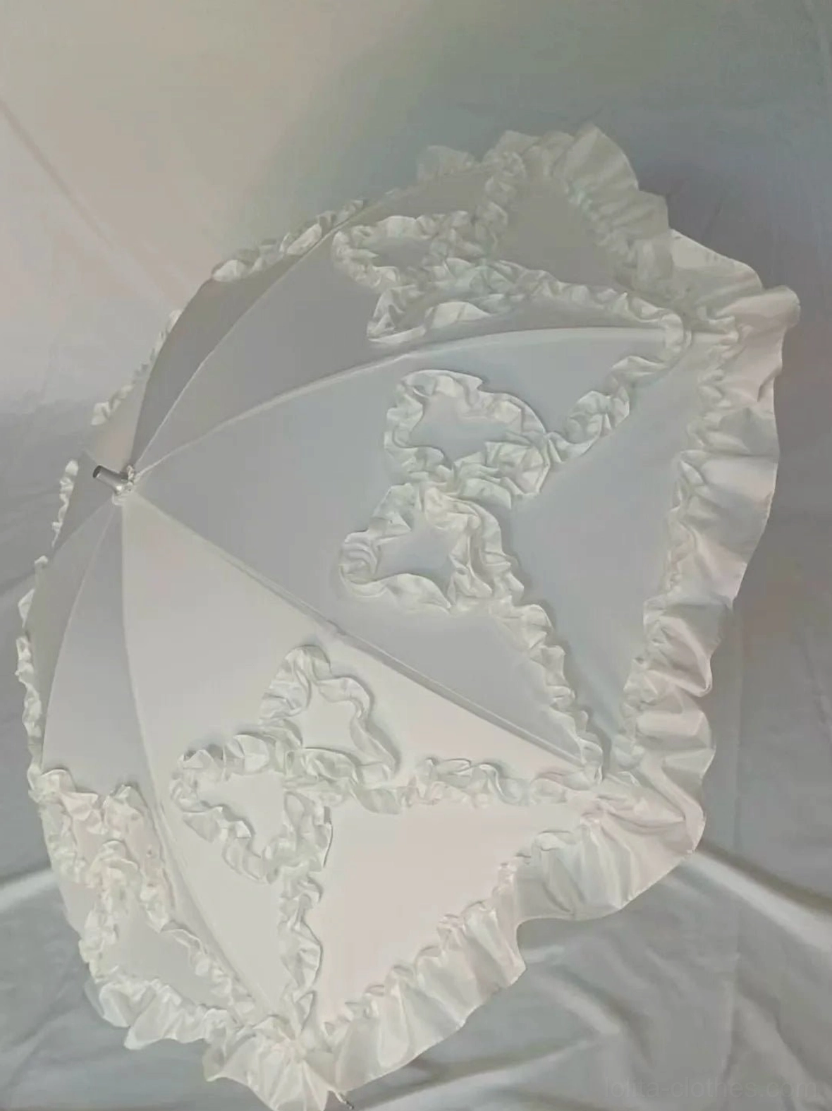 Milky white bow-shaped ruffled Lolita parasol with delicate bow-trim details and ruffled canopy, studio flat lay view on neutral background showcasing sweet style