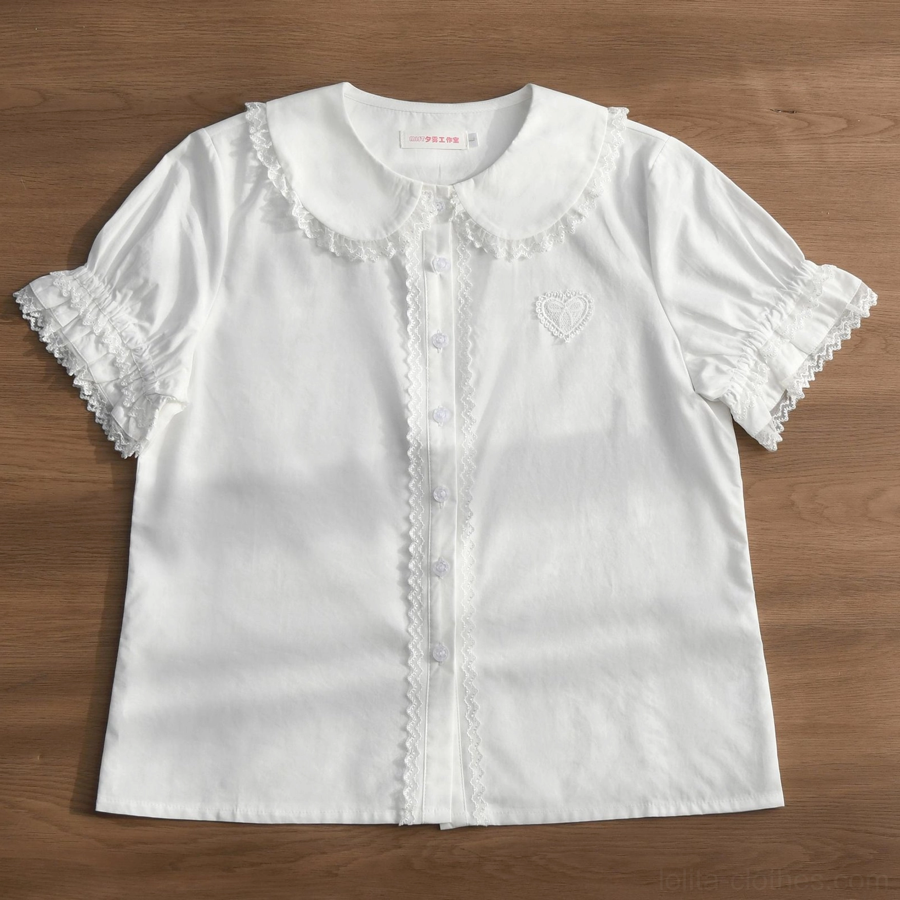 Pure white Lolita blouse with lace-trimmed Peter Pan collar, ruffled sleeve cuffs and heart embroidery on wooden tabletop