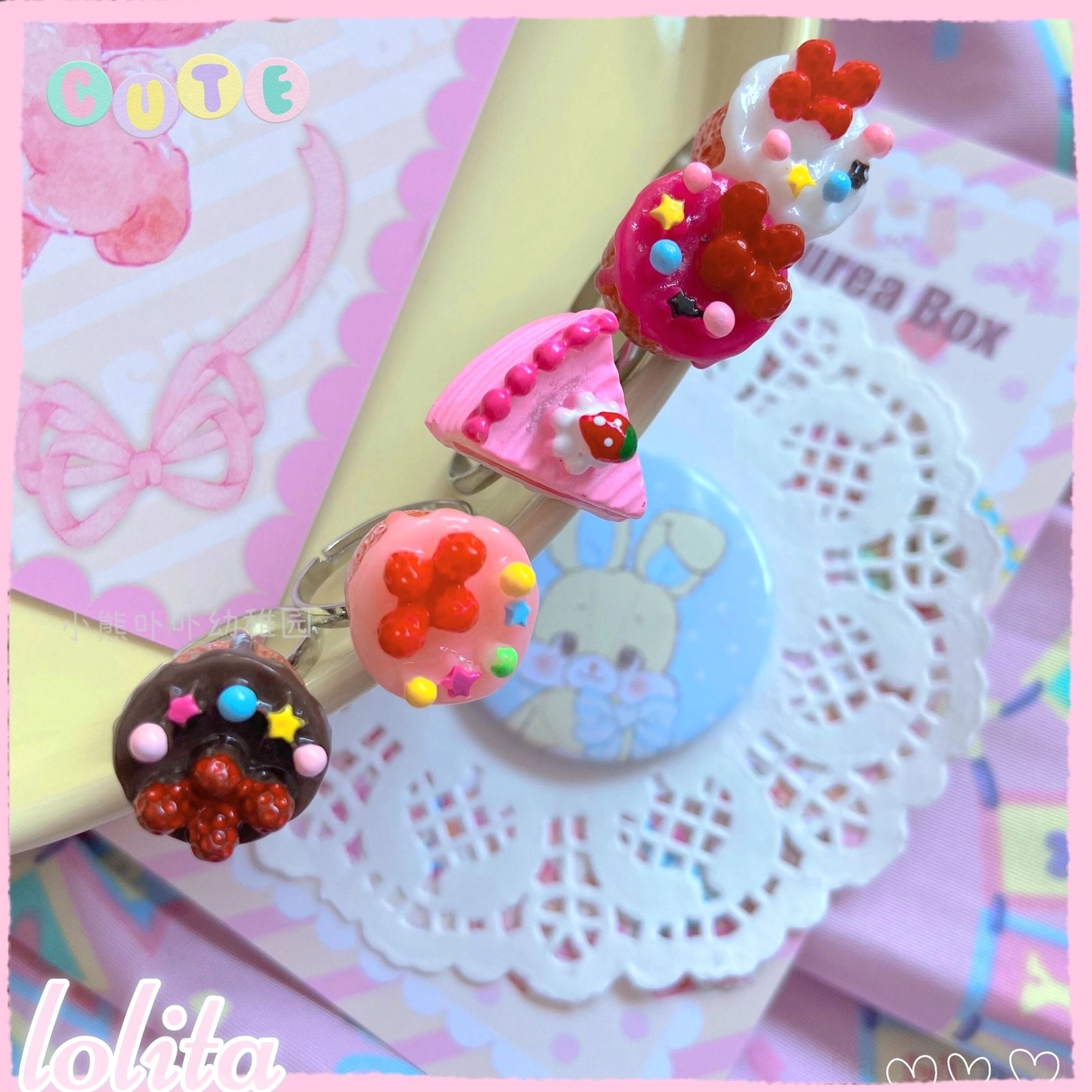 Close-up cluster of glossy miniature cupcake lolita rings with bead toppings and vibrant red pink frosting details on white doily mat