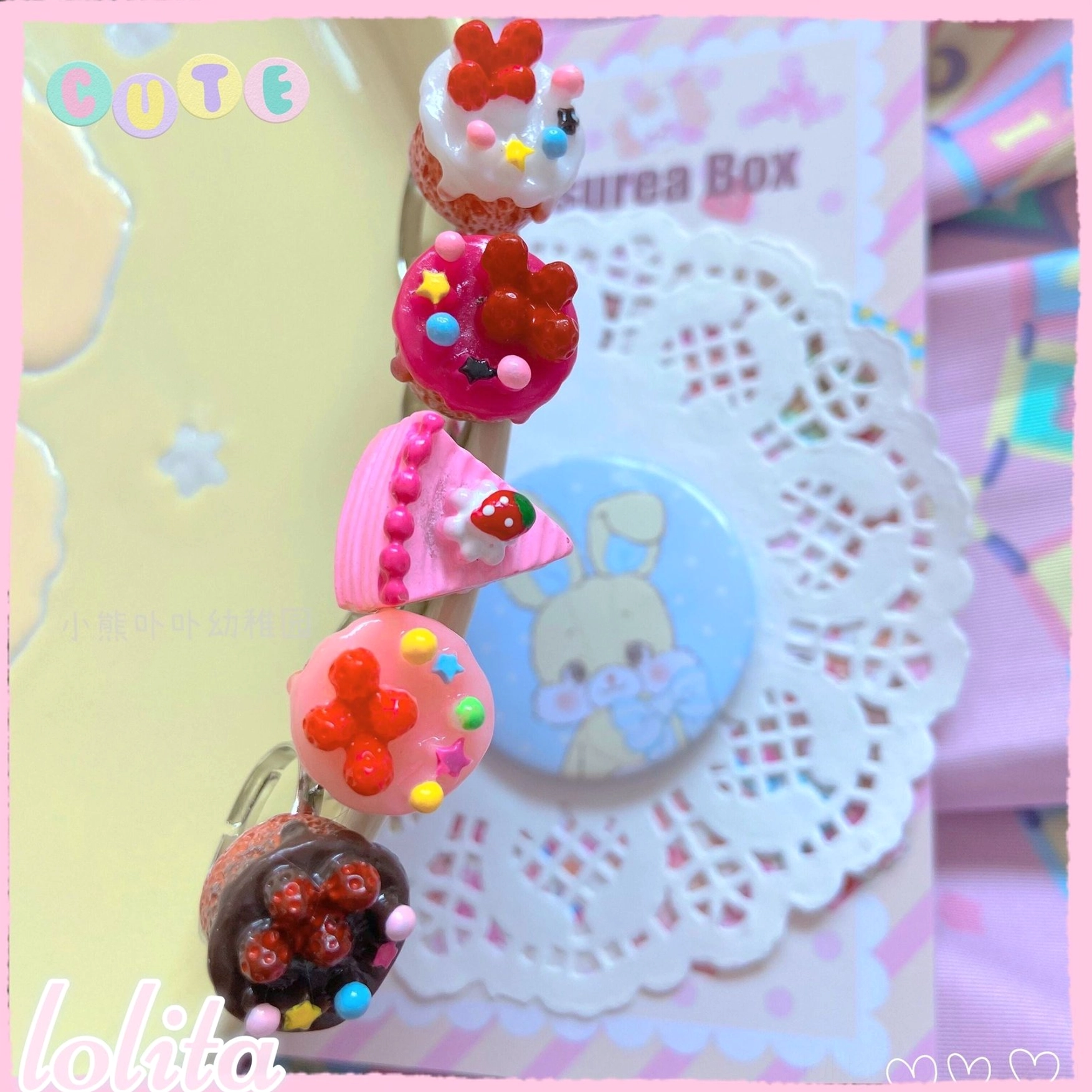 High-angle close-up of miniature cupcake lolita rings with glossy frosting and decorative beads in varied cupcake styles on white doily mat