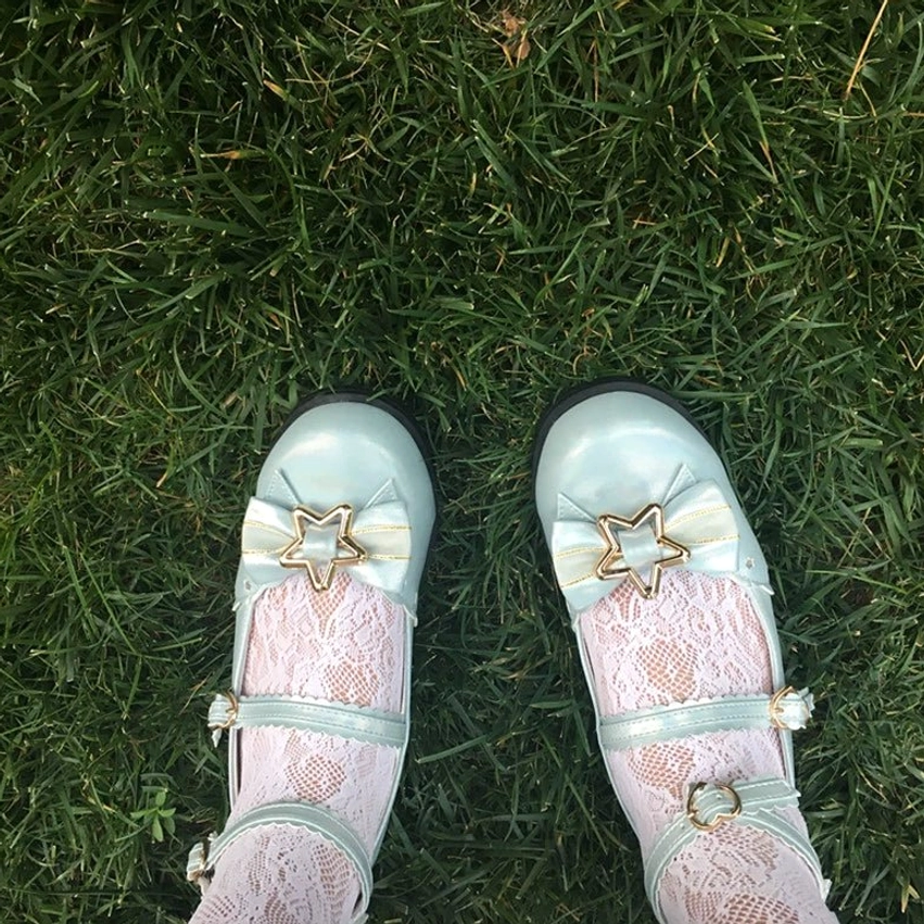 Top-down overhead view of mint blue sweet lolita shoes worn with crisscross sheer lace socks on grass showing double ruffled ankle straps star gold hardware low flat heel