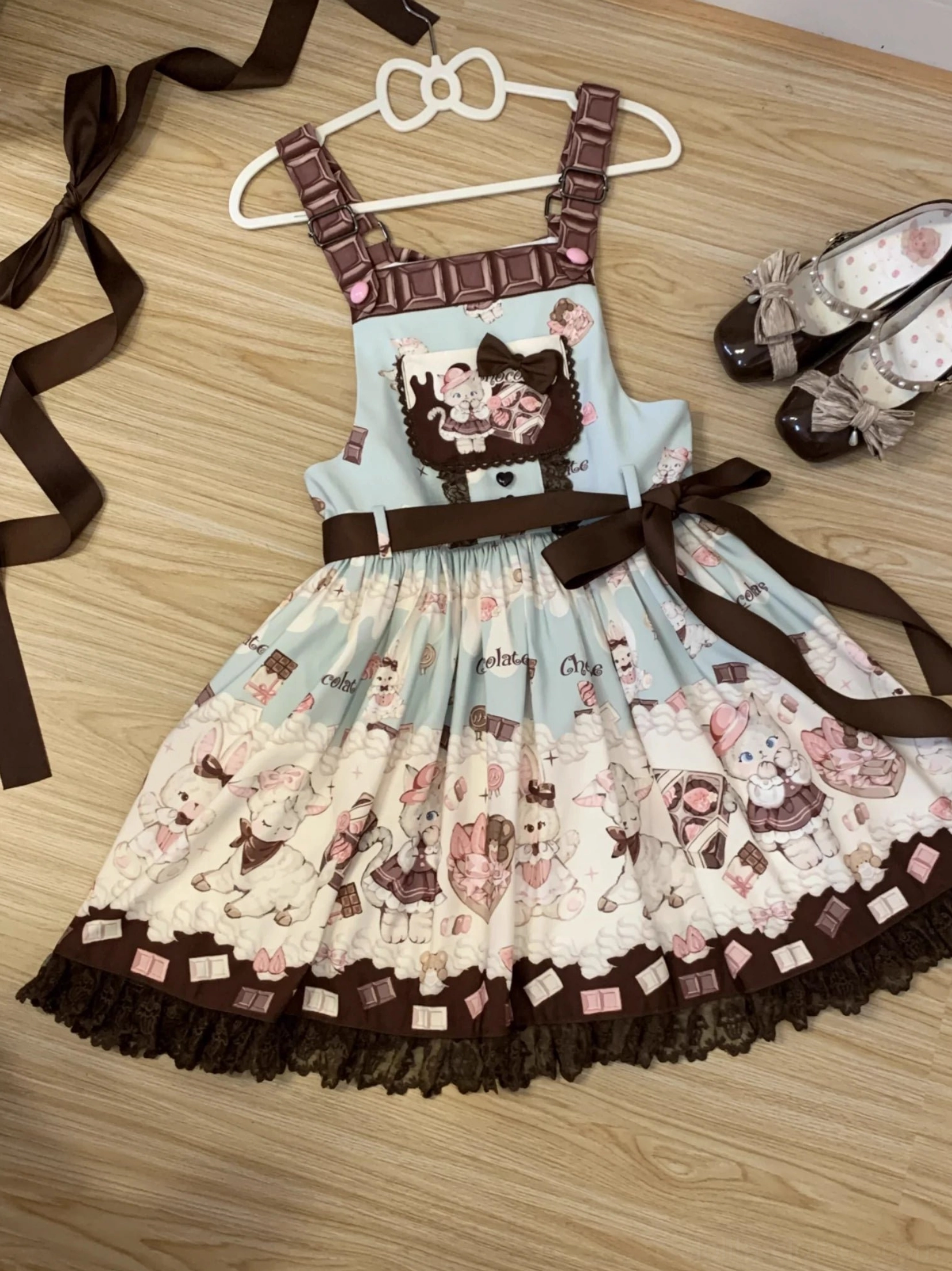 Mint green cat print Lolita salopette dress displayed in flat lay on wooden floor with detachable long straps, lace hem detail, waist bow decoration, and coordinating sweet Lolita Mary Jane shoes