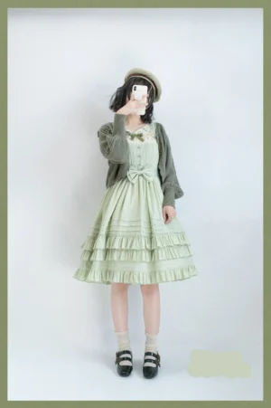 Mint green lolita JSK dress with layered ruffle skirt, lace yoke, waist bow sash, paired with cropped cardigan, boater hat and mary jane shoes studio photo