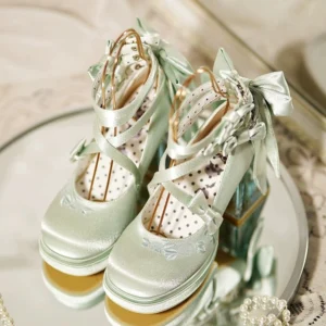 Pair of mint green Lolita high heel shoes displayed on round mirror tray, top-down flat lay view showing polka dot insole, cross straps with satin bows, and delicate floral embroidery