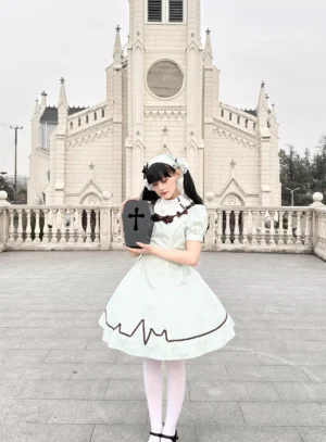 Full front view of mint and white striped Old School Lolita OP dress worn in European church square setting, styled with white lace maid headpiece, white stockings, and vintage cross clutch accessory