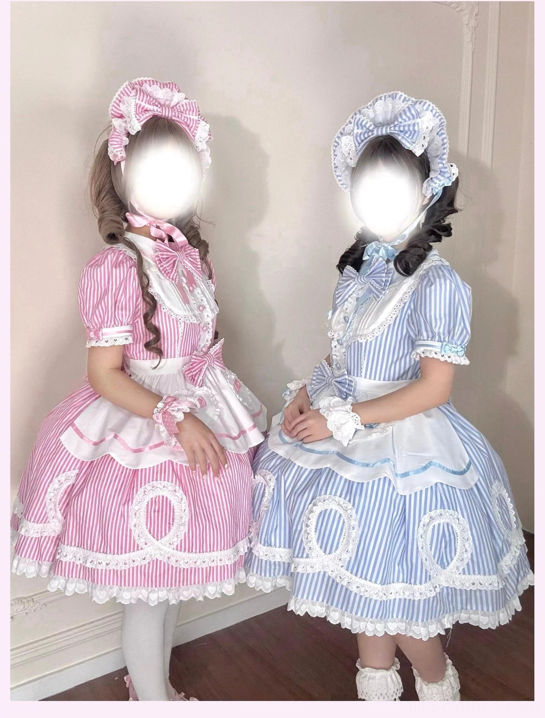 Model in pink striped lolita OP dress with heart-shaped button cuffs and detachable apron showing hand accessories