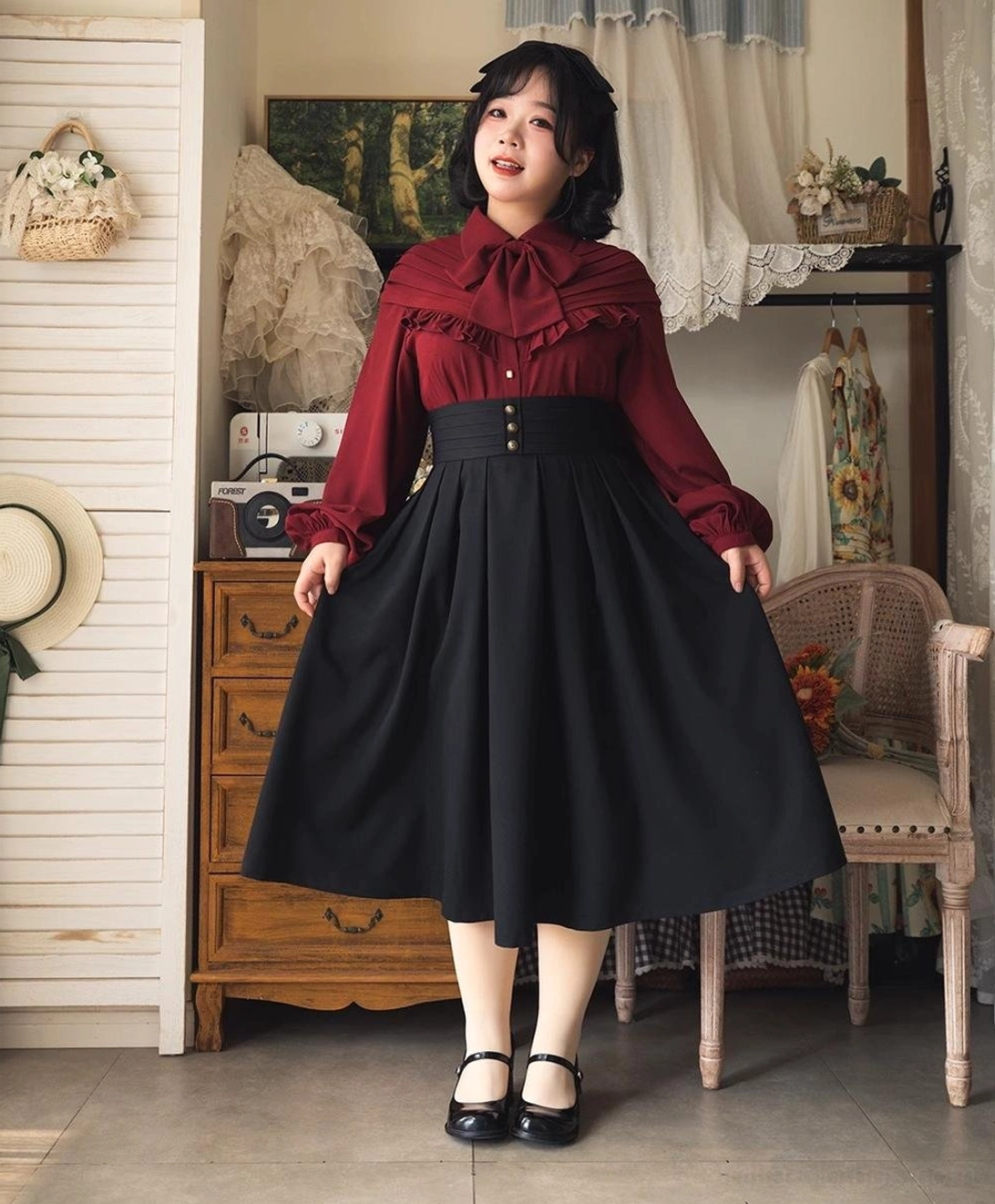 Female model wearing burgundy vintage Lolita bow blouse and black midi skirt set with Mary Jane shoes and sheer stockings in retro boutique studio, front full body posing showing ensemble fit