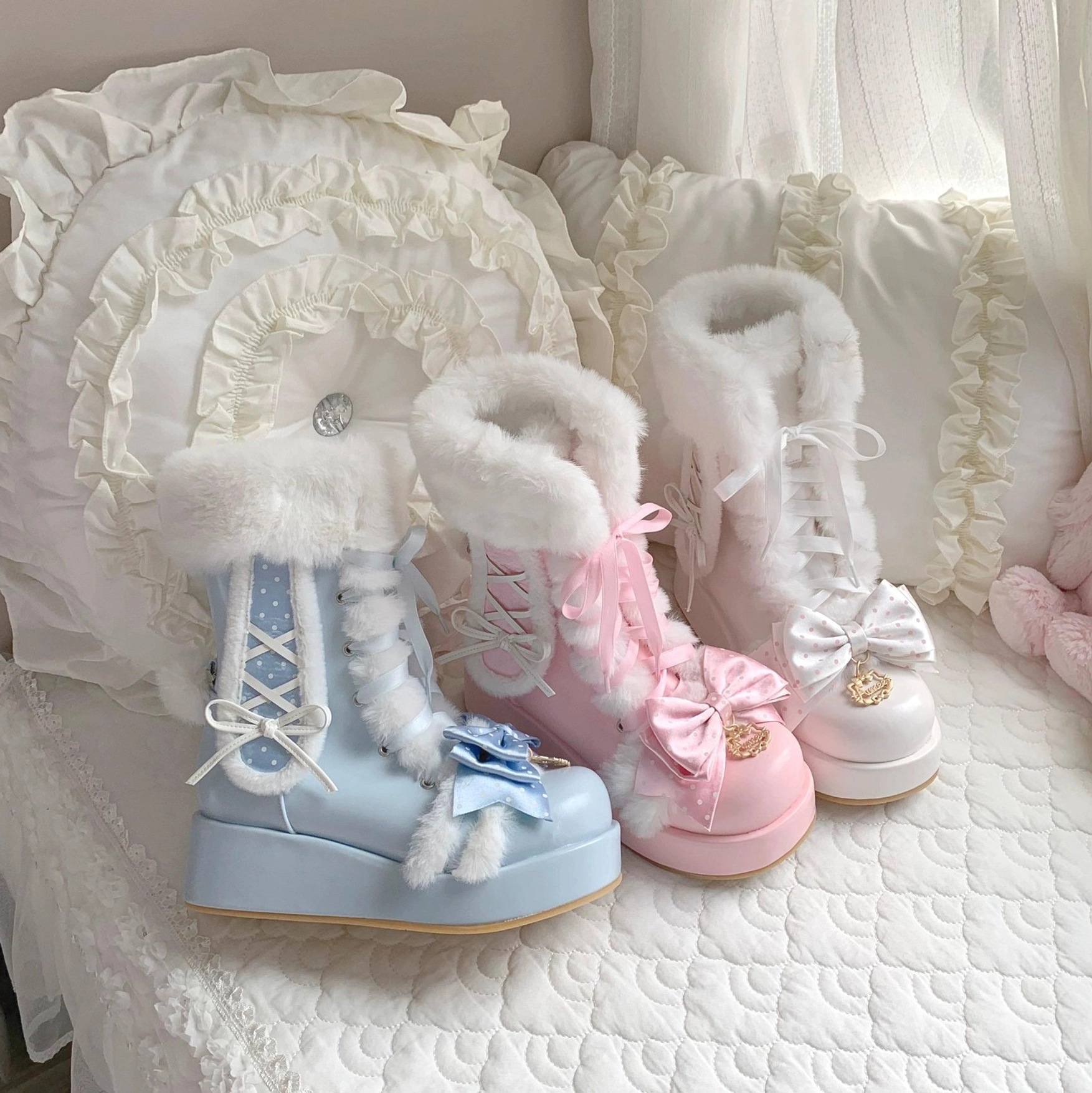 Overhead flat lay of multi-color sweet lolita bunny ear platform boots on bedroom bedding, showing furry trim, lace-up design, decorative bows, and pink blue white colorways