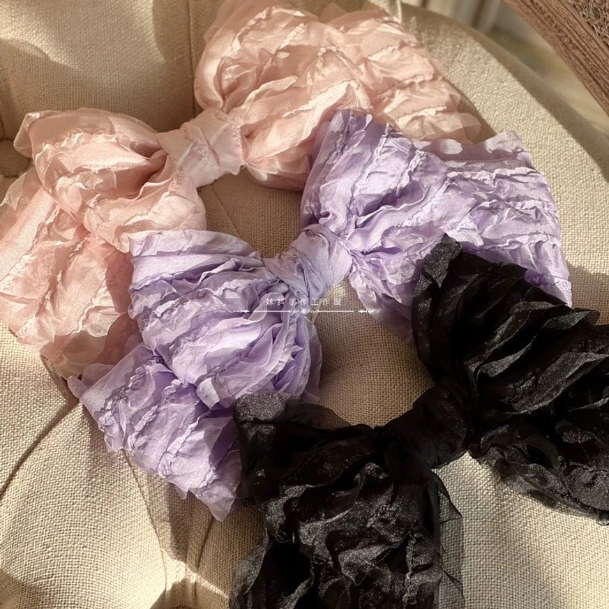 Multi-color ruffled organza lolita hair clips in pink light purple and black flat lay on beige fabric surface