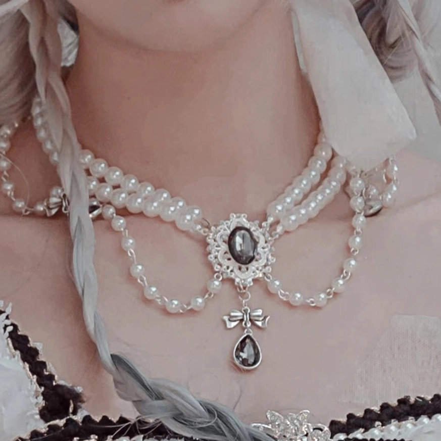 Multi-layered pearl bridal necklace featuring gemstone centerpieces, tassel chains, teardrop dark gem pendants, and decorative pearl strands displayed on model's neckline in close-up frontal view showing delicate jewelry layering