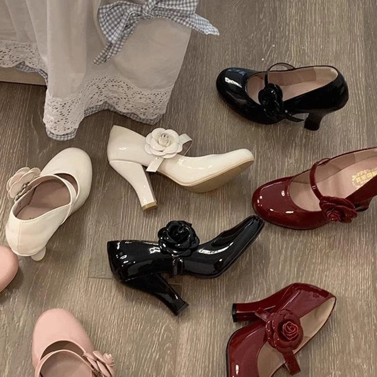 Multiple color Lolita Mary Jane high heel shoes overhead flat lay on wooden floor with lace curtain decor black burgundy off-white flower strap decorations vintage aesthetic