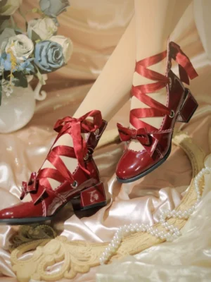 Wine red glossy patent leather lolita lace-up block heel shoes with round toe and decorative front bow, shown on model's feet from three-quarter overhead angle against vintage satin backdrop
