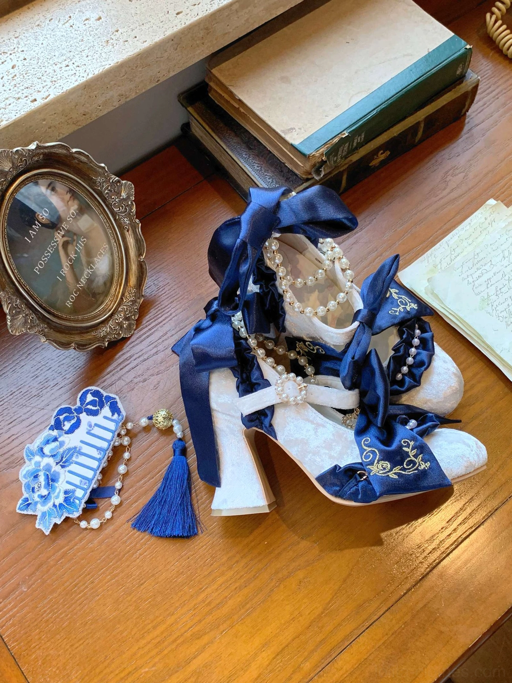 Navy blue block heel classic Lolita wedding shoes with pearl decorations worn by seated model in ruffled blue dress and floral stockings
