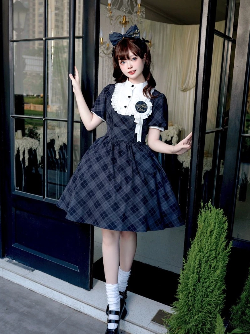 Navy blue dark tartan plaid lolita OP dress with ruffled collar brooch detail and short puff sleeves three-quarter view at luxury indoor doorway with chandelier